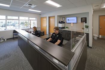 Two people sitting at a reception desk in a well-lit office.