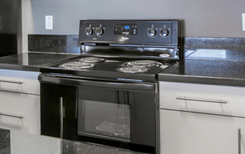 A black stove top oven with four burners and a digital display is on a kitchen counter.