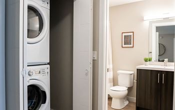 A white washing machine is in a small bathroom with a toilet and sink.