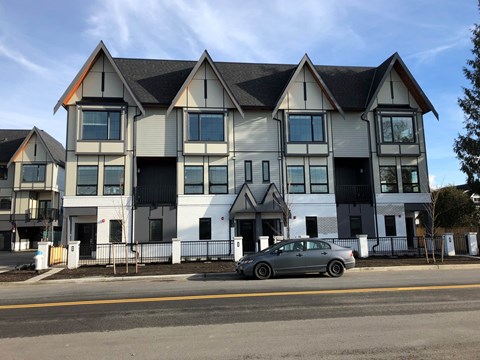 A grey car is parked in front of a white and grey building.