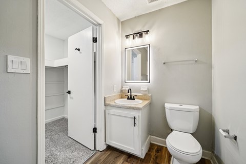 A white bathroom with a toilet, sink, mirror, and a door.