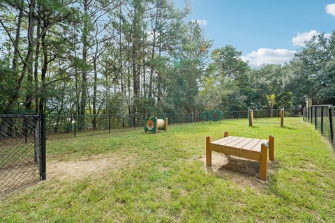 A wooden bench sits in the middle of a grassy area with trees in the background.