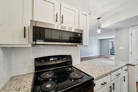 A black stove top oven with four burners is in a kitchen with white cabinets.