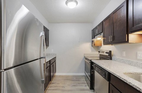 A kitchen with a stainless steel refrigerator and dark brown cabinets at The Onyx Hoover Apartments, Hoover, AL
