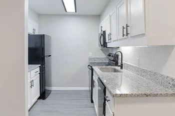 A kitchen with a black fridge, white cabinets, and granite countertops. at The Onyx Hoover Apartments, Hoover, 35216