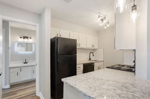 A black refrigerator sits in a kitchen with white cabinets and a marble countertop at The Onyx Hoover Apartments, Alabama, 35216