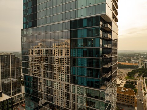 A tall glass building stands in the foreground with a cityscape in the background.