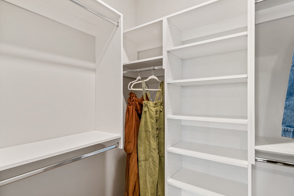 a walk in closet with white shelves and a closet door open with clothes hanging