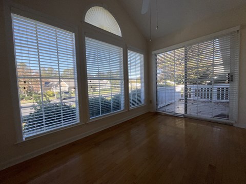 A room with wooden floors and a large window with blinds.
