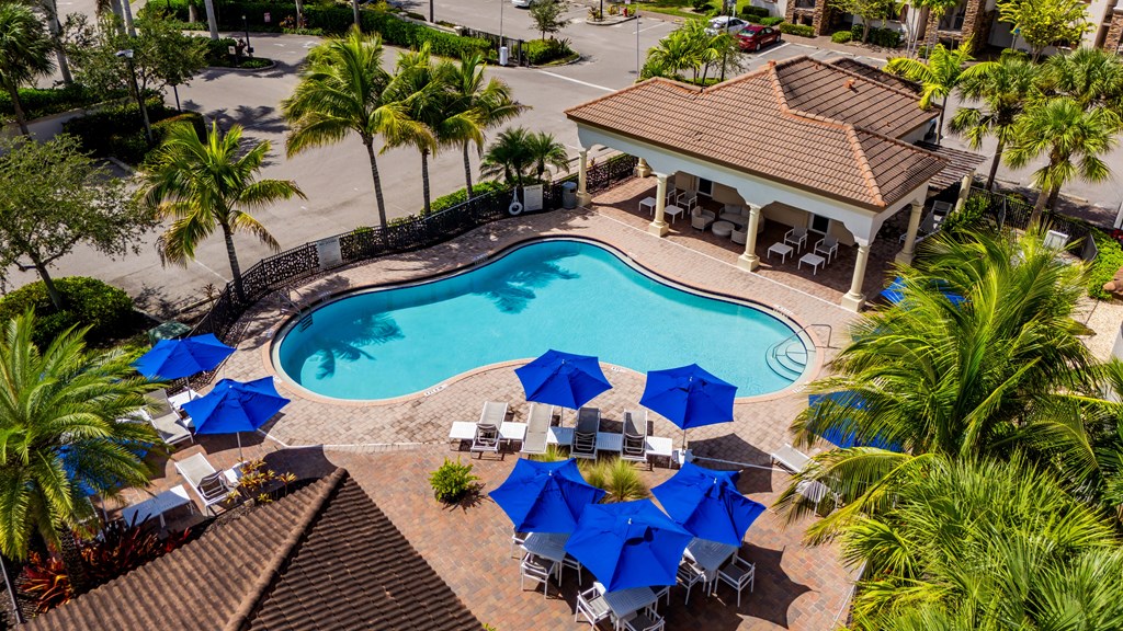 A pool surrounded by blue umbrellas and palm trees.