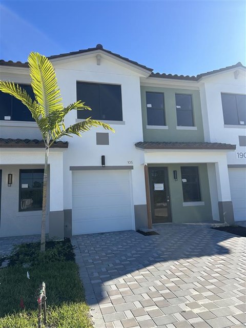 A white house with a green door and a palm tree in front.