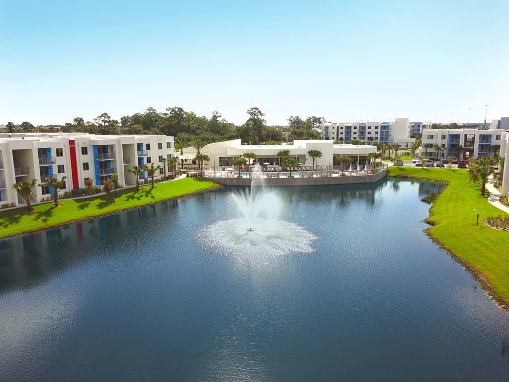 Lake with fountain surrounded by Icon One Daytona apartments on the left and right and clubhouse and pool centered at Icon One Daytona, Daytona Beach, FL