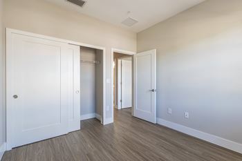 A room with white walls and wood flooring, featuring a white door and a closet with a white door.