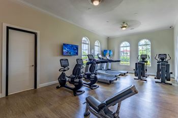 A spacious home gym with a variety of exercise equipment and a flat-screen TV mounted on the wall.