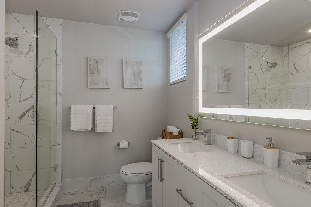 A bathroom with a marble shower, white toilet, and a white sink.