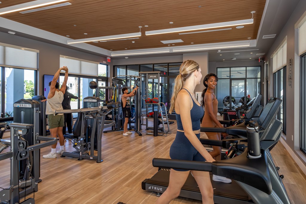 A woman is running on a treadmill in a gym with other people working out.