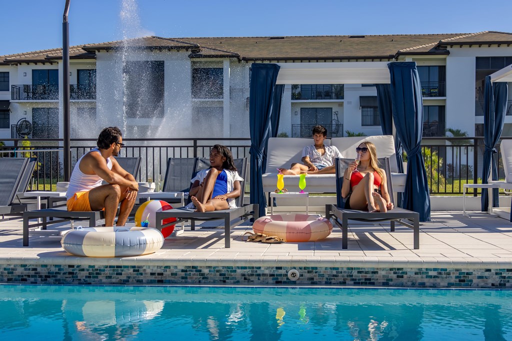 Four people are sitting by a pool with a waterfall in the background.