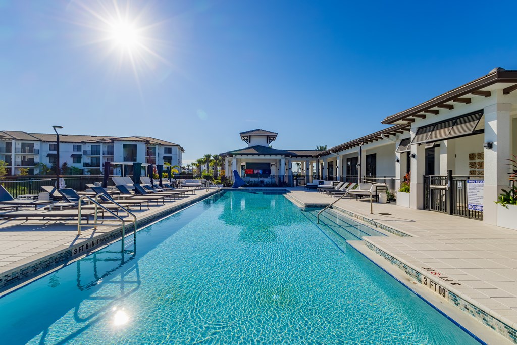 A sunny day at the pool with chairs and buildings in the background.