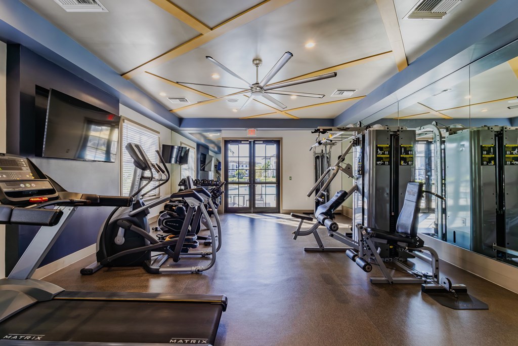 A gym with treadmills, elliptical machines, and a ceiling fan.