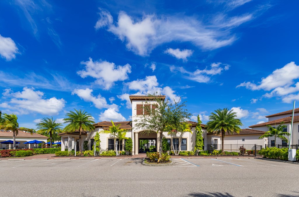 A building with a tower-like structure in the center of a parking lot with palm trees in the background.