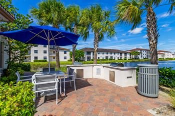 A patio with a table and chairs under an umbrella with a view of a body of water and buildings in the background.