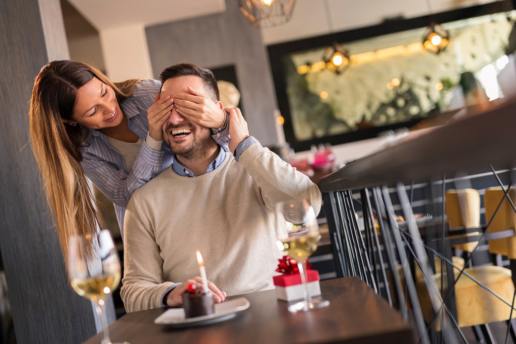 a woman covering a mans eyes in a restaurant