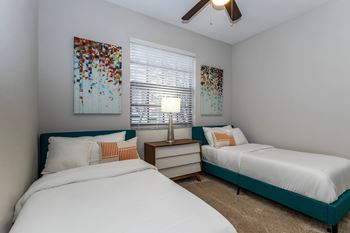 A bedroom with two beds, one with a blue headboard, and a ceiling fan.