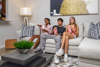 Three people are sitting on a couch with popcorn and watching television.