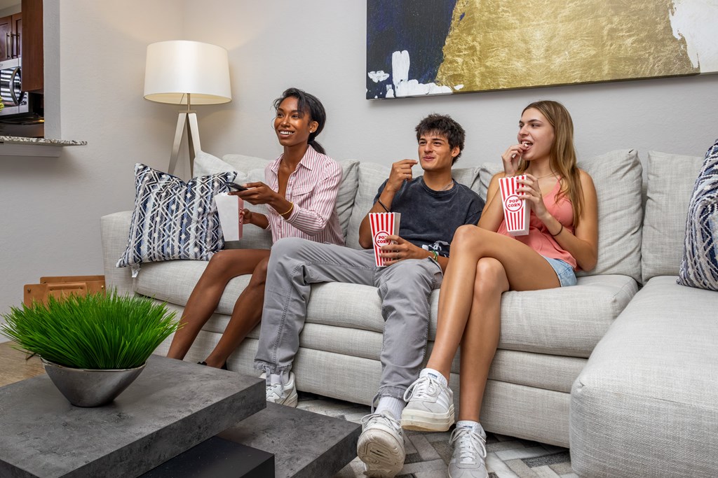 Three people are sitting on a couch with popcorn and a remote control.