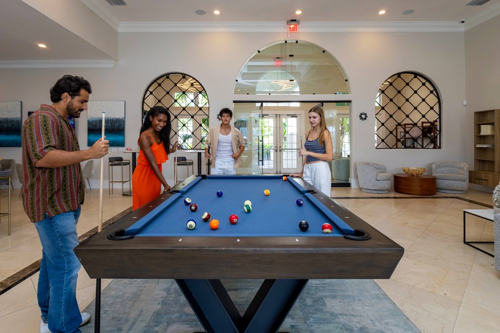 Four people are playing pool in a room with arched windows.