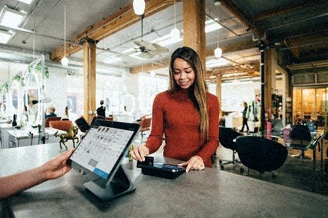 a woman sitting at a table with a person holding a tablet