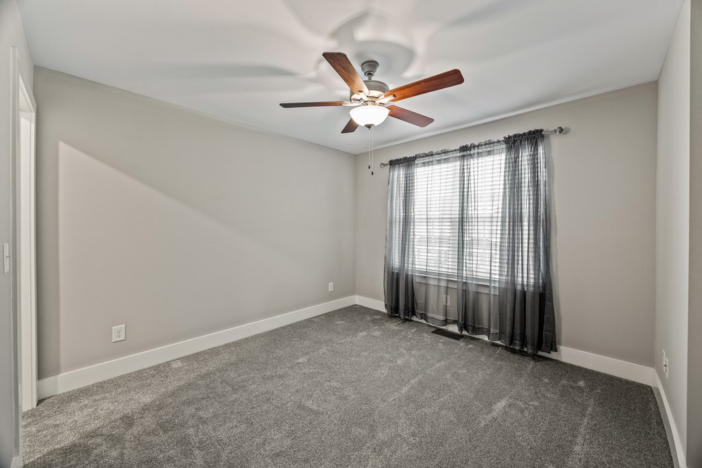 A room with a ceiling fan and carpeted floor.