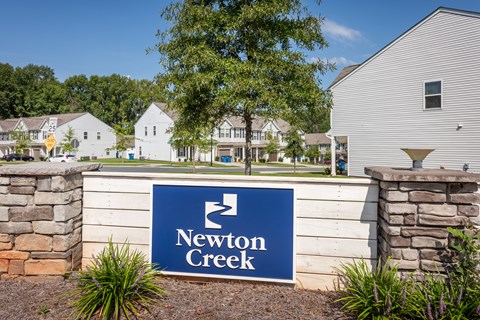 A sign that says Newton Creek in front of some houses.