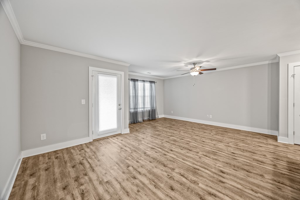 A room with a ceiling fan and light, hardwood floors, and a window with curtains.