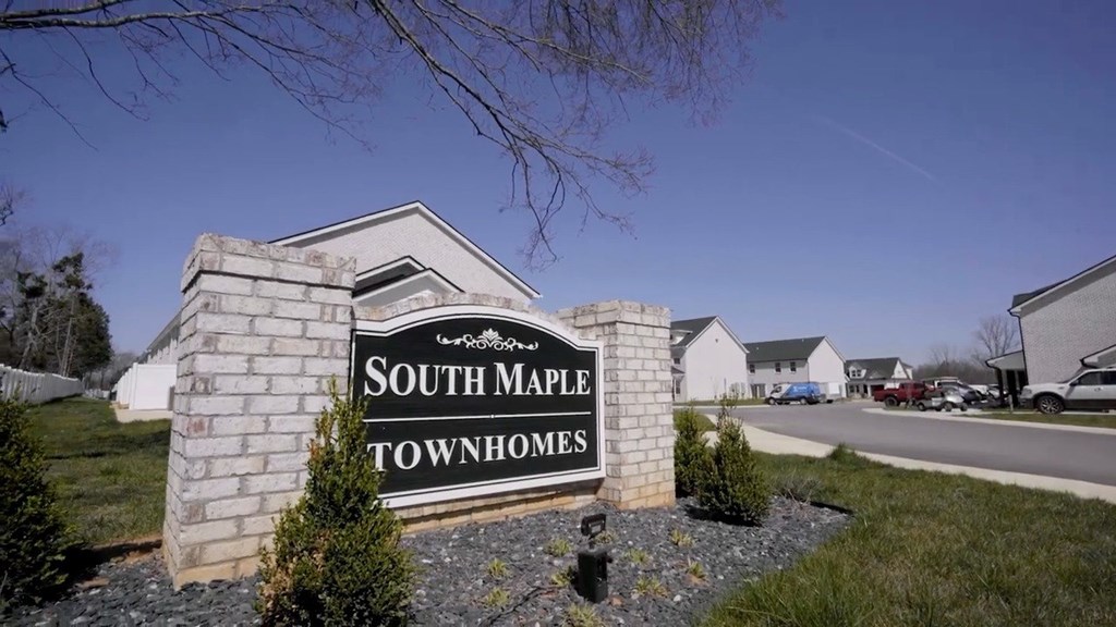 A sign that says South Maple Townhomes stands in front of a grassy area.
