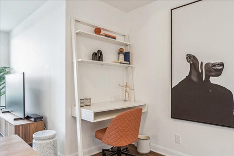 A room with a desk, chair, and a painting on the wall.