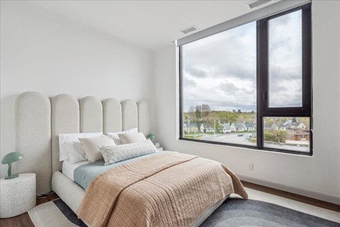 A bedroom with a large bed and a view of the outside through a window.