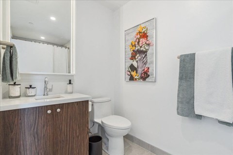 A bathroom with a toilet, sink, mirror, and a picture of flowers on the wall.