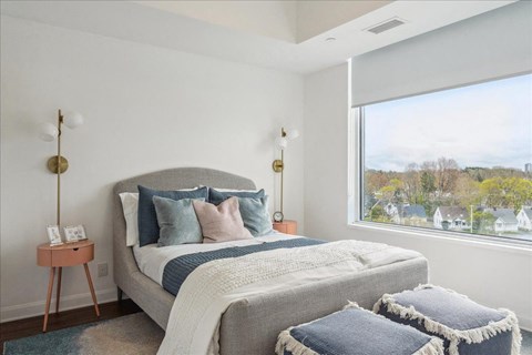 A bedroom with a large bed and a view of houses outside the window.