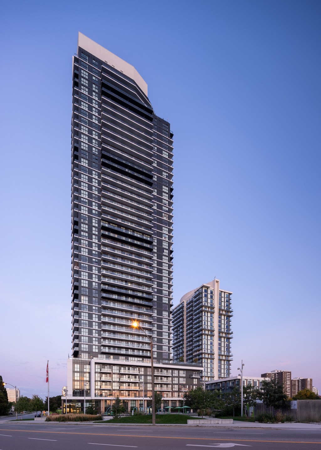 A tall, modern building with a curved top stands in the foreground with a clear blue sky above.