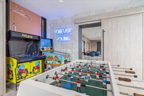 A foosball table is in the middle of a room with a DJ booth to the left and a doorway to another room to the right.