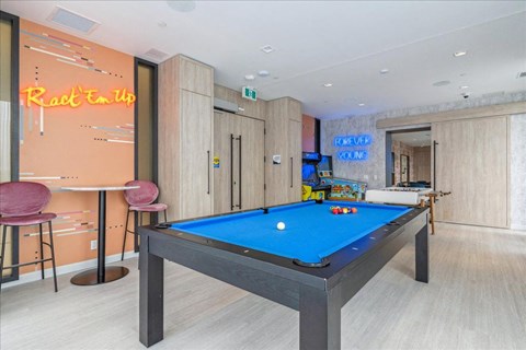 A pool table is in the middle of a room with a bar and a neon sign that says "Rat Trap Up".