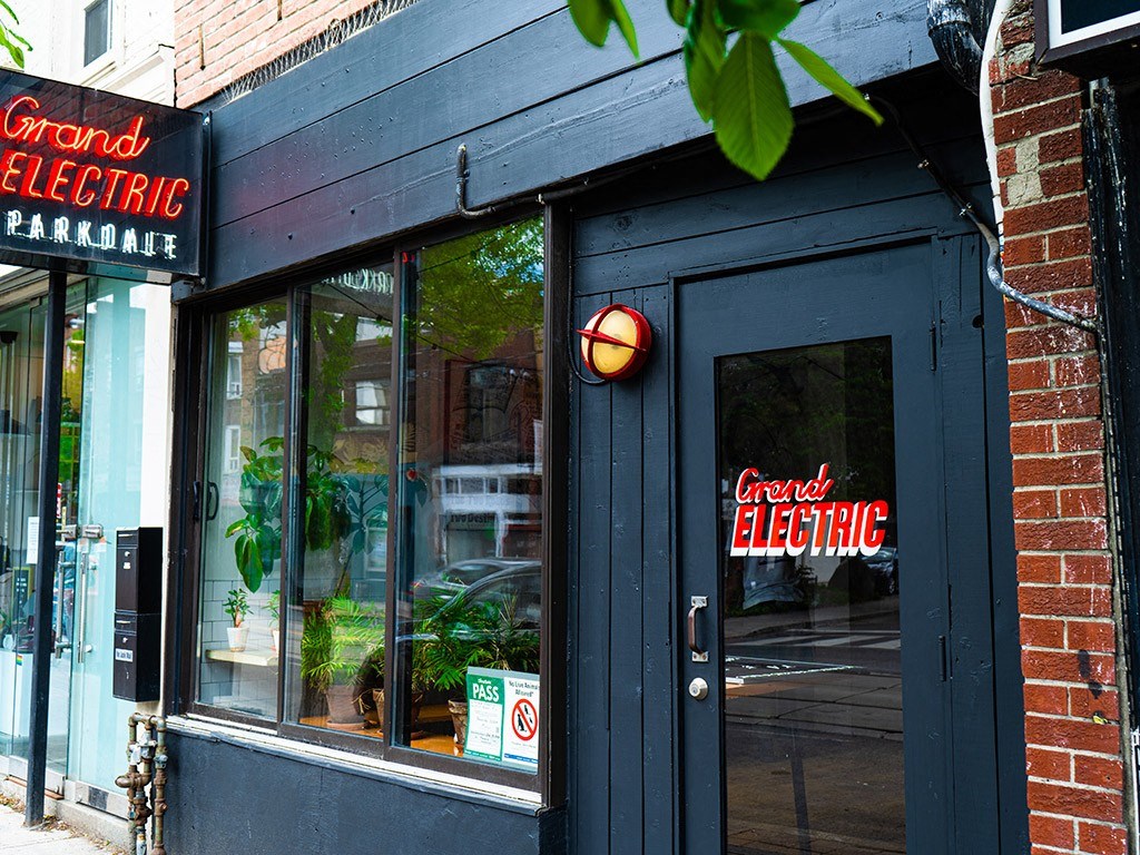 the front of a store with a black door and a red electric sign