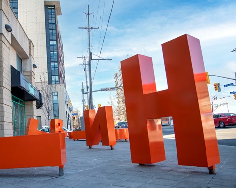 A large orange sculpture of the letter H is in the foreground of a city street.