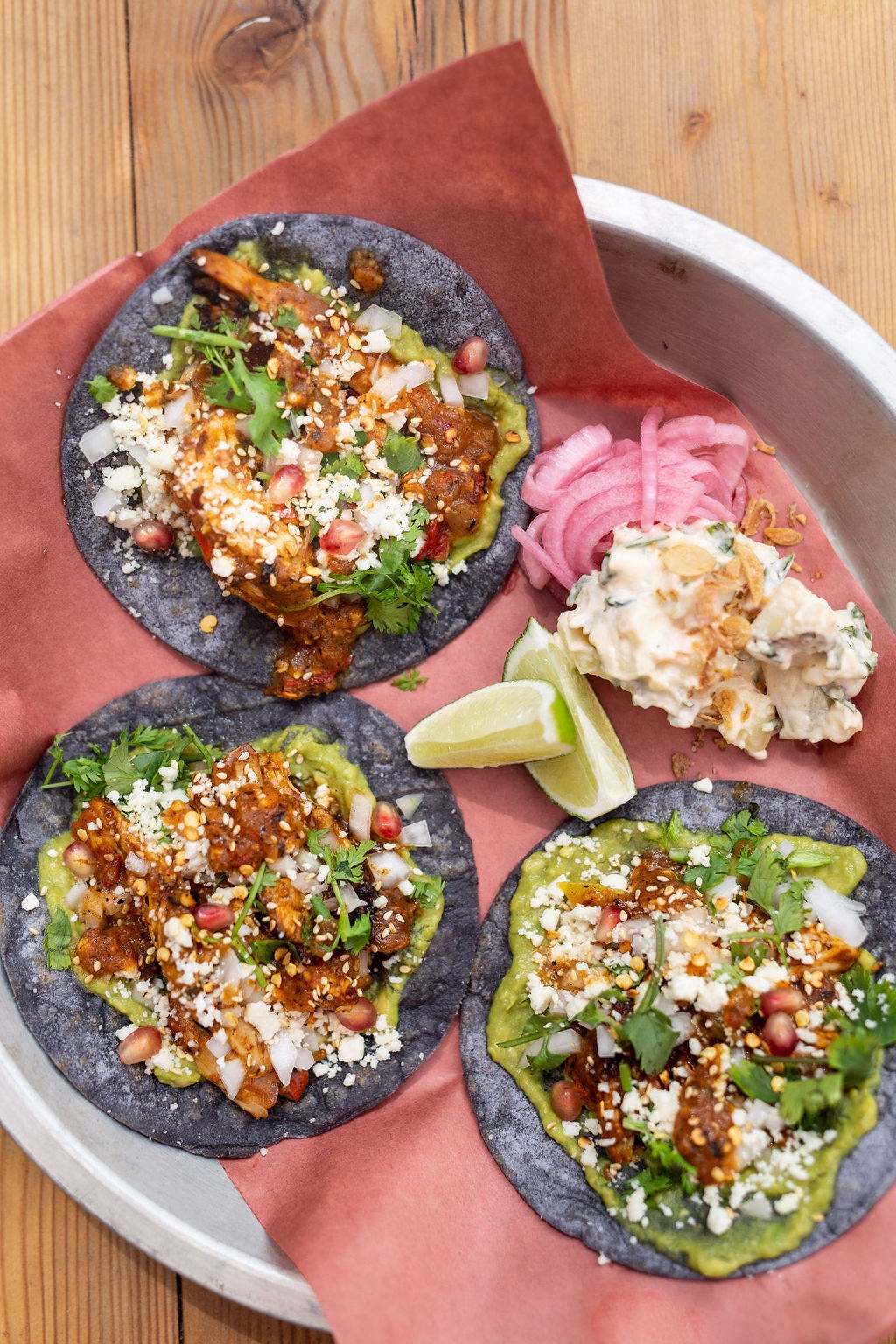 three tacos on a plate with 2 wedges of lime