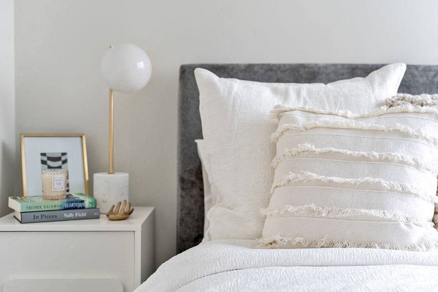 a white bed with white pillows and a white nightstand with a white lamp