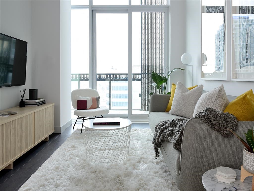 A living room with a grey couch, a white rug, and a TV on a wooden cabinet.