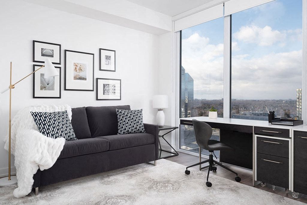 A black couch with a white blanket sits in front of a window with a view of a cityscape.