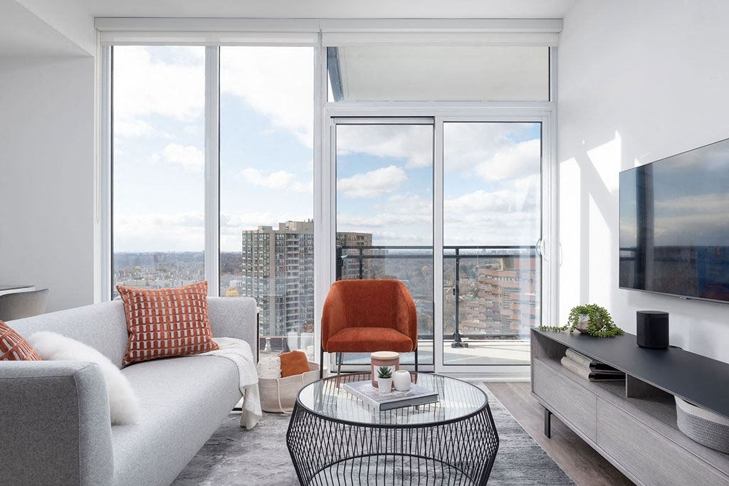 A modern living room with a grey couch, a red chair, and a glass table.