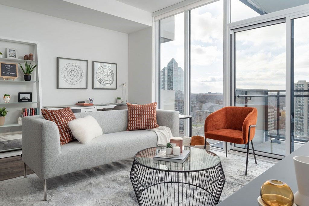 A grey couch with red pillows sits in a modern living room with a view of the city.